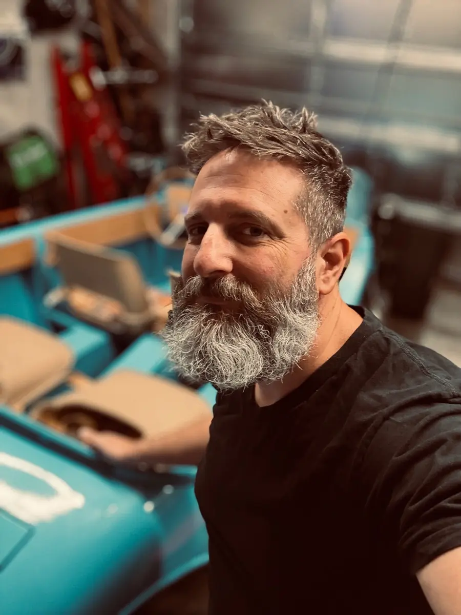 Brian Schneider, welder and fabricator, in his garage with a classic boat project behind him