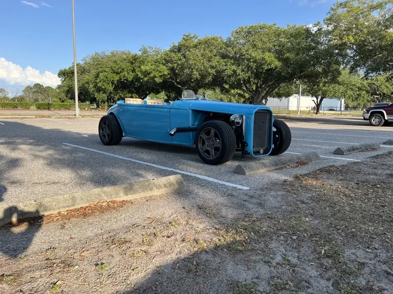 Blue hotrod roadster parked outdoors under oak trees
