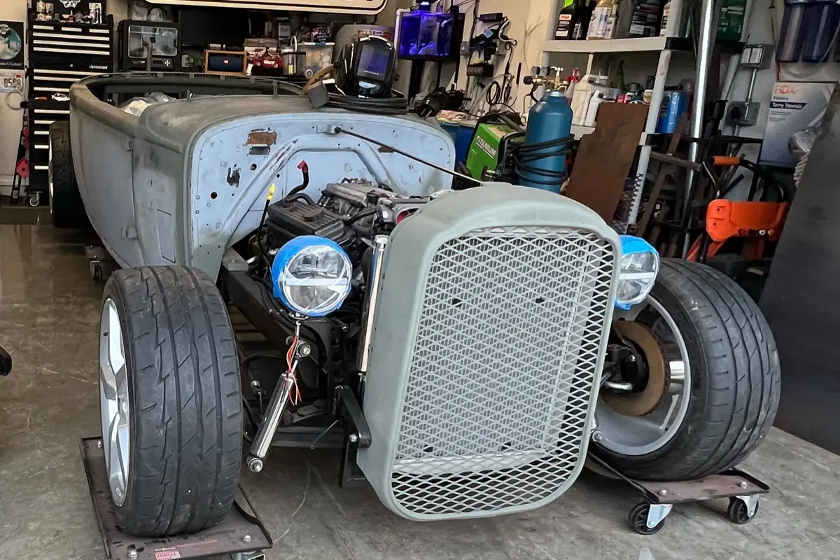 Hotrod roadster in the shop with exposed engine, mesh grille and custom front suspension